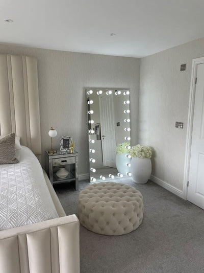 Keira Full Length Hollywood Mirror XXL with bright bulbs in elegant bedroom setting, featuring beige decor and plush ottoman.