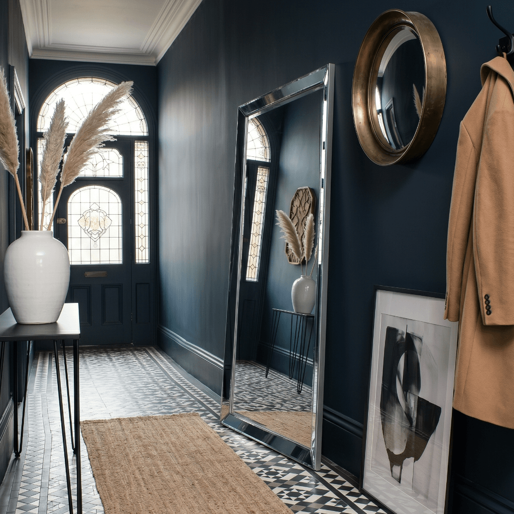 Full length silver bevelled leaner mirror in navy blue Victorian hallway with encaustic floor tiles, pampas grass and camel coat — Hollywood Mirrors UK