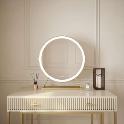 Anne Round Hollywood Mirror Gold 60x63cm with customizable lighting and touch sensor controls sits on a white and gold textured desk with a reed diffuser, candle, and glass lantern against a cream-colored wall.