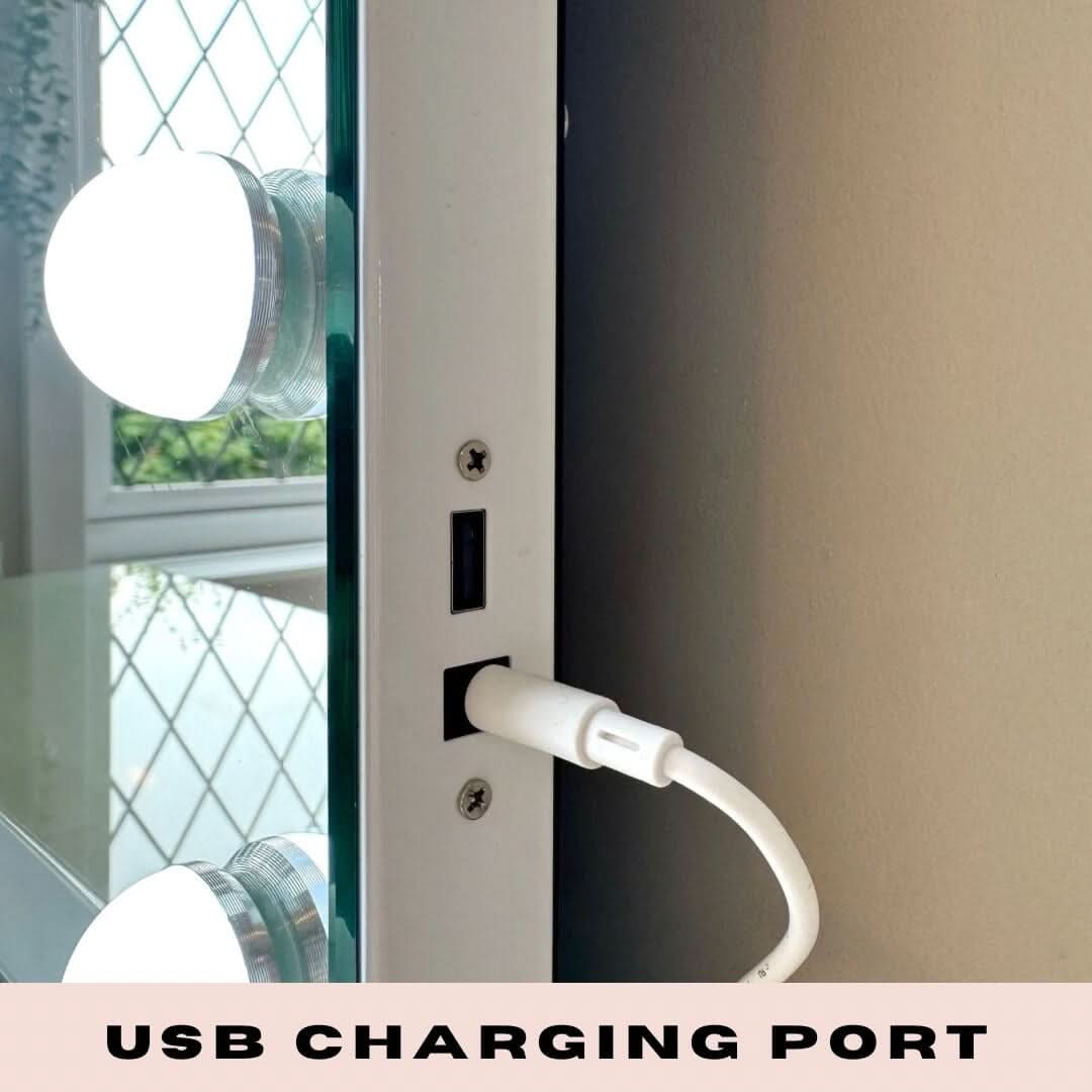 Close-up of a white USB charging cable plugged into the side port of the Margot Small Hollywood Mirror 50x42cm with vanity lights, adjustable brightness, and USB CHARGING PORT text displayed at the bottom.