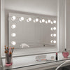 The hollywood mirrors Nicole Hollywood Mirror Wall Mounted 100x60cm features a glass tabletop displaying makeup brushes in a pink holder, an eyeshadow palette, powder compact, lipstick, and a pink perfume bottle.