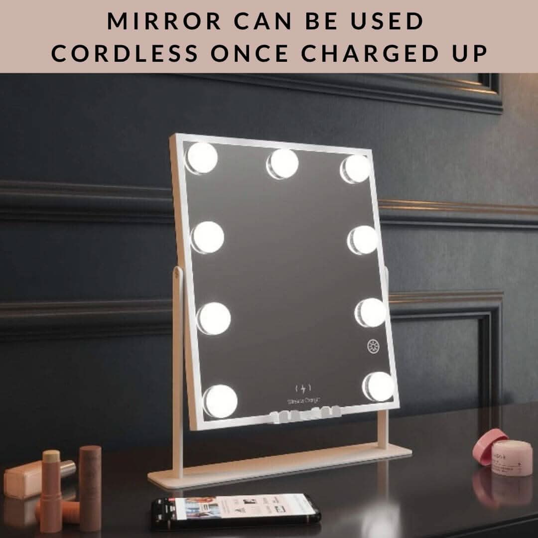 The Renée Bluetooth Hollywood Mirror 30x25cm, with built-in LED bulbs, sits on a table with cosmetics and a smartphone. Text above reads: Mirror can be used cordless once charged up.