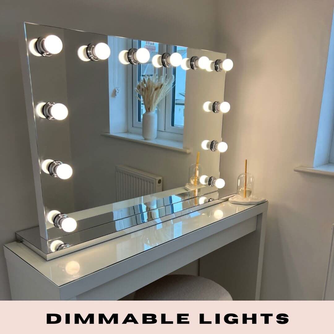 The Scarlett Large Hollywood Mirror 100x70cm by hollywood mirrors is a white vanity table with a large rectangular mirror framed by round dimmable LED bulbs. It includes a matching stool, glass decor piece, dried flowers, and DIMMABLE LIGHTS text at the base.