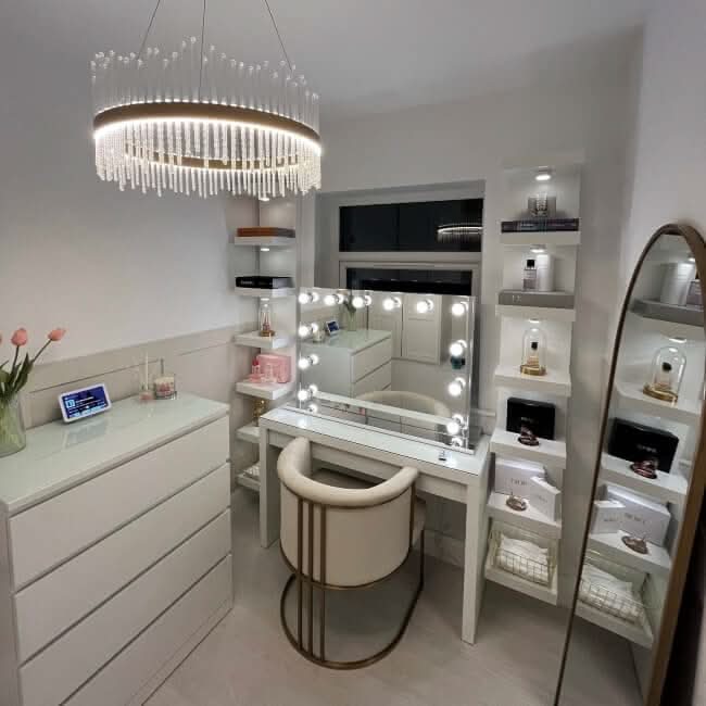 A modern, well-lit vanity area featuring the Scarlett Large Hollywood Mirror 100x70cm by hollywood mirrors, plush chair, beauty shelves, tulip-adorned dresser, round chandelier, and tall standing mirror.
