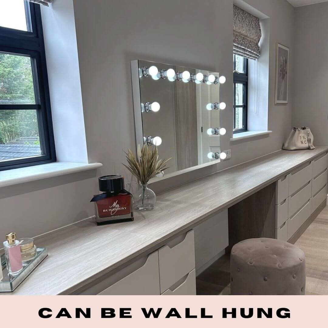 The Scarlett Large Hollywood Mirror 100x70cm by hollywood mirrors features LED bulbs and a stylish mirrored wall with round lights. Set above a long makeup vanity with windows on the left, it includes a cushioned stool and can be wall hung.