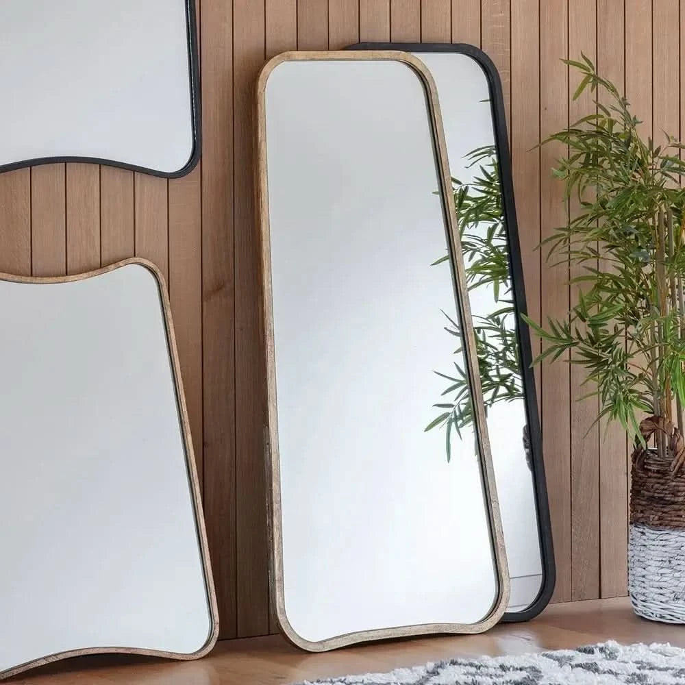 Three large The Valentina Gold Mirror Full Length Mirrors by hollywood mirrors (123cm x 56.5cm) with gold frames lean against a wood-paneled wall; a green potted plant and a patterned rug are also visible nearby.