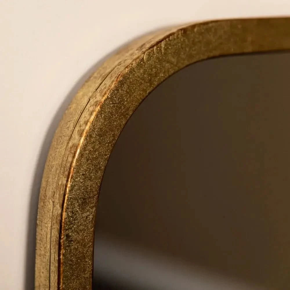 Close-up of The Valentina Gold Mirror Full Length Mirror (123cm x 56.5cm) by hollywood mirrors, featuring a rectangular shape with rounded edges and a textured gold frame, set against a light-colored wall.