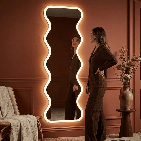 Woman standing in front of a decorative mirror with wavy frame in a room with a pink wall.