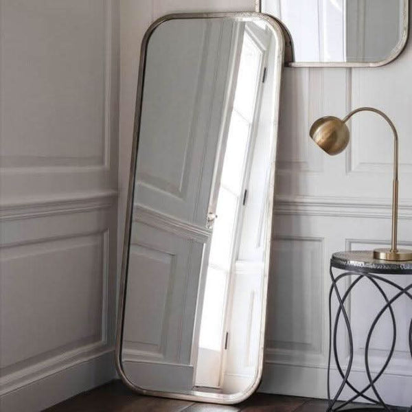 Distressed Champagne Leaner Mirror with streamlined metal frame, enhancing elegant home décor next to a brass lamp.
