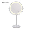 The Pre Order Mid June Illuminated Round Cosmetic Mirror has a 20cm diameter, a chrome adjustable stand, and features a circular warm LED light around the edge. Warm Light is displayed in the top left corner. Rechargeable design.