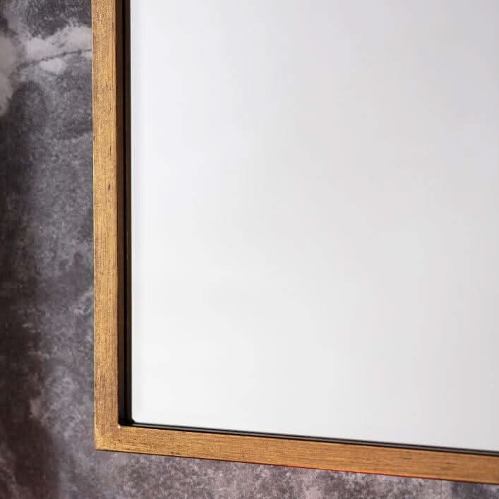 Close-up of Moira antique gold arch mirror frame on a textured wall, highlighting the minimalist thin metal design.