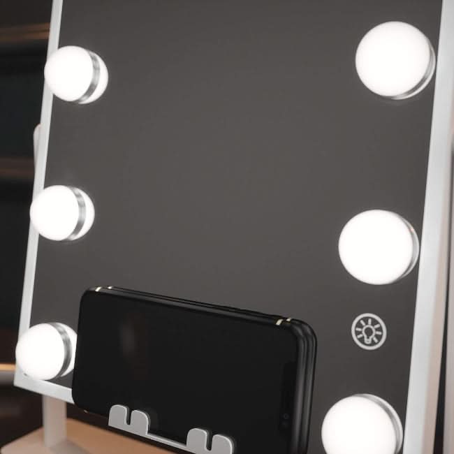 The Renée Bluetooth Hollywood Mirror 30x25cm features six LED bulbs around the edges, a bottom-center smartphone holder, and a touch sensor button on its sleek surface.