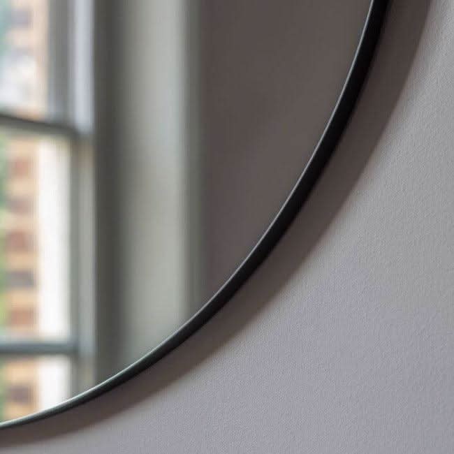 Close-up of Scandi Large Round Mirror with slim black metal frame, near window, showcasing modern industrial design, 80cm diameter.
