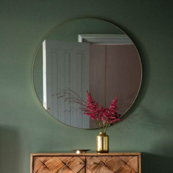 Scandi large round mirror with champagne metal frame, 80cm, wall hanging on green wall, reflecting room interior.